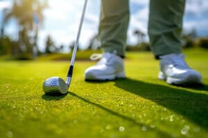 Cropped close-up view of a male golfer’s legs and head of his golf club on the green
