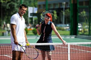 Smiling younger couple pausing at the net on a tennis court